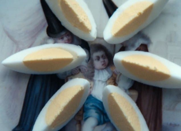 severance-whipping-boy-theory: A photo of an antique plate with a design featuring a young boy and two older people holding the boys arms. On top of the plate is a hard-boiled egg cut evenly into six pieces.